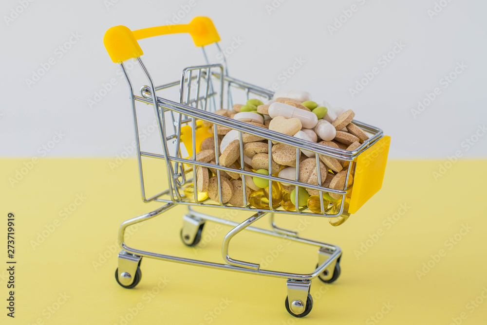 small shopping cart on yellow white background with pills