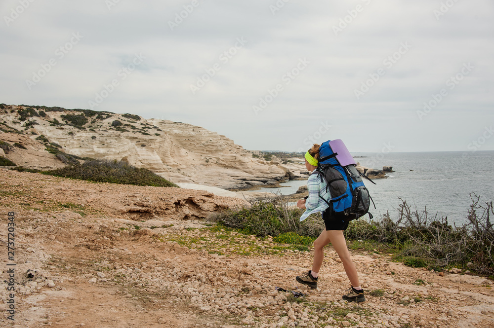 Girl walking on the rocks with hiking backpack on the sea coast