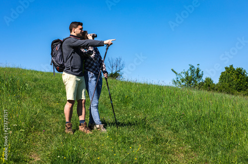 Young couple enjoying hiking together in nature standing on the top of the hill talking and looking at horizon. 