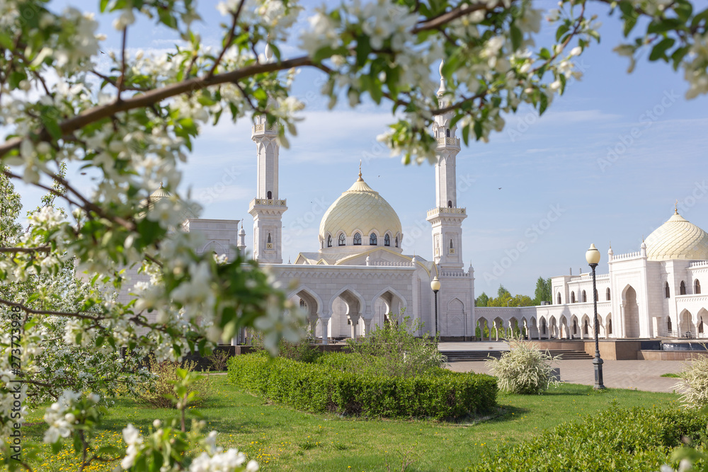 White mosque of the Bulgarians on a sunny spring day against the backdrop of blossoming apple tree branchesapple are out of focus
