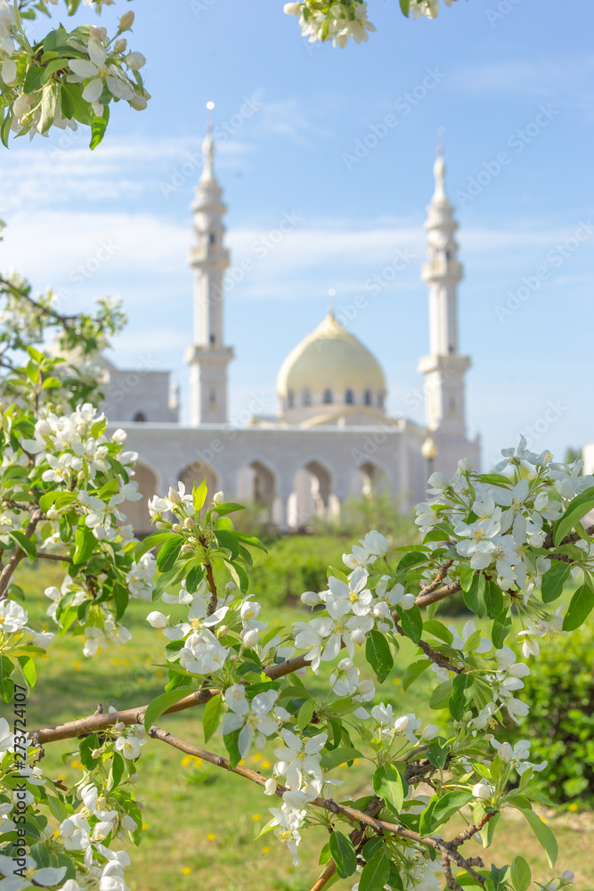 The White Mosque of the Bulgarians is out of focus on a sunny spring day against the backdrop of the blossoming apple tree branches