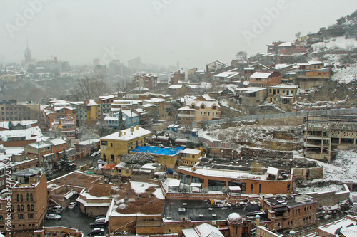 View of Tbilisi Old town Sololaki in winter while snow.  Orange snowy roofs, orthodox church, river Kura make atmosphere of the city. Georgia Country.