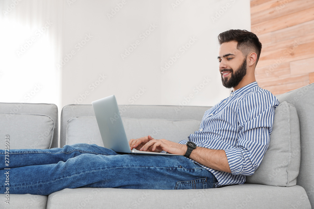 Handsome young man working with laptop on sofa at home Handsome young man working with laptop on sofa at home