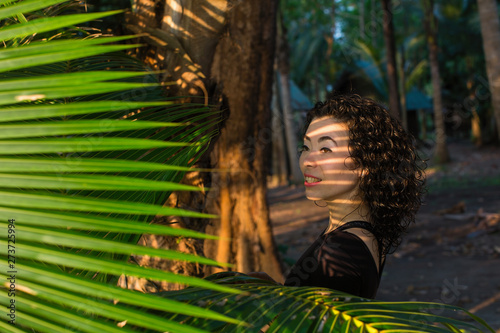 Asian girl looks through the palm leaves.. photo