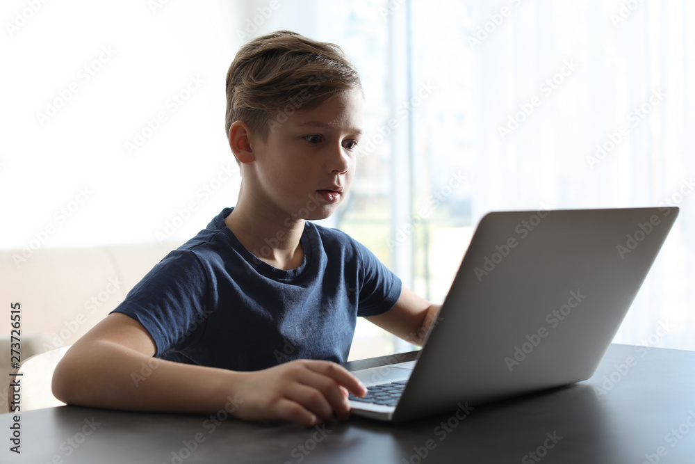 Shocked little child with laptop at table indoors. Danger of internet