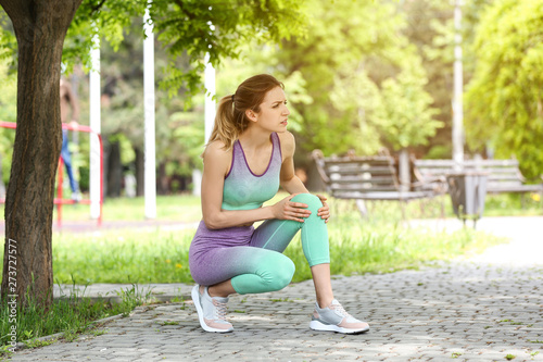 Young woman suffering from knee pain in park