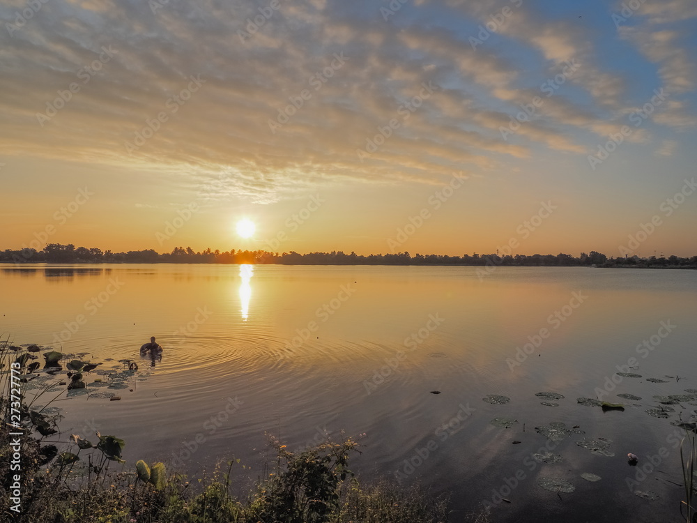 Lake view morning scenic a fisherman floating in water with red sun light and blue sky background, sunrise at Krajub Lake, Ban Pong, Ratchaburi, Thailand. Lake view morning scenic a fisherman floating in water with red sun light and blue sky background, sunrise at Krajub Lake, Ban Pong, Ratchaburi, Thailand.