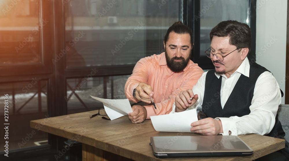 Two business men discussing financial documents while sitting at the table in the office.