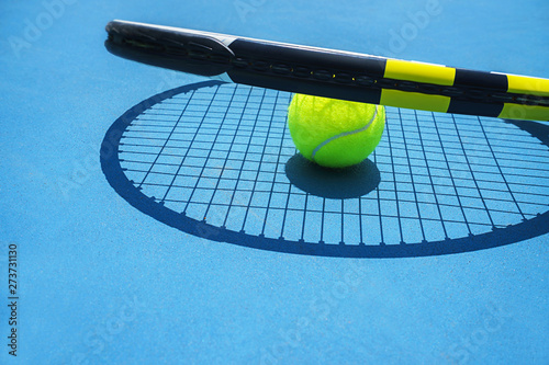 Summer sport concept with tennis ball and racket on blue hard tennis court. Top view, copy space. Blue and yellow. © IrynaV