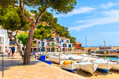 Young couple of people walking in port of Llafranc village with fishing boats on beach, Costa Brava, Spain