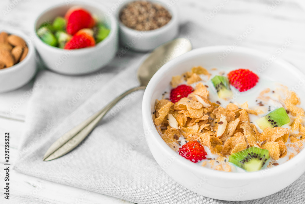 Bowl of breakfast cereals with milk, strawberry, kiwi, almonds, and granola seeds against white rustic wooden background. Concept of healthy breakfast food, clean eating, and dieting.