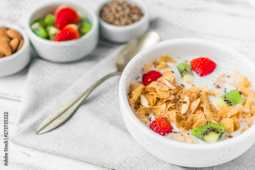 Bowl of breakfast cereals with milk, strawberry, kiwi, almonds, and granola seeds against white rustic wooden background. Concept of healthy breakfast food, clean eating, and dieting.