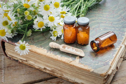 Chamomile flowers, bottles of homeopathic globules and old books. photo