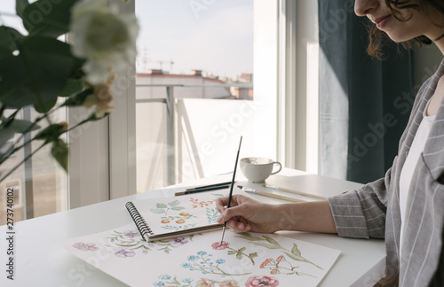 Crop person hand with brush painting watercolor flowers on large sheet at desk photo