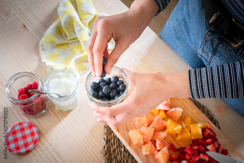 Anonymous woman taking blueberries from jar while cooking healthy vitamin food from fresh fruits at home