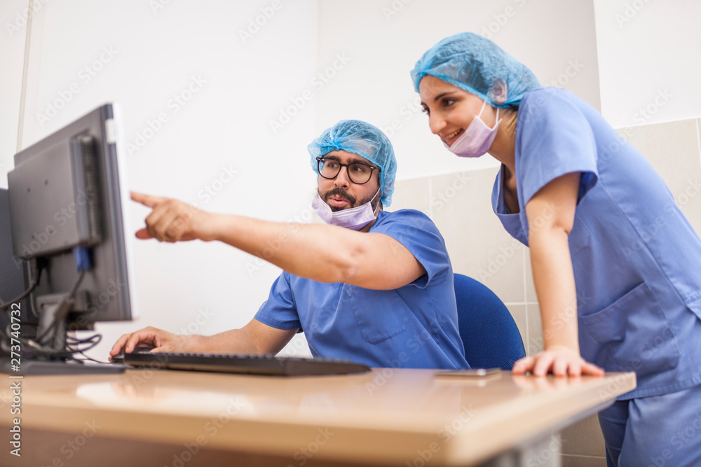 Team of surgeons, man and woman using the computer before the surgery and committing the details Team of surgeons, man and woman using the computer before the surgery and committing the details