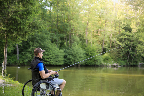 Happy and young disabled or handicapped man fishing at a lake in nature. Popular sport for paraplegics.