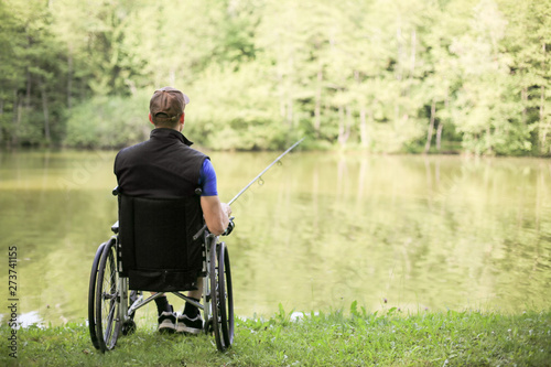 Happy and young disabled or handicapped man fishing at a lake in nature. Popular sport for paraplegics.