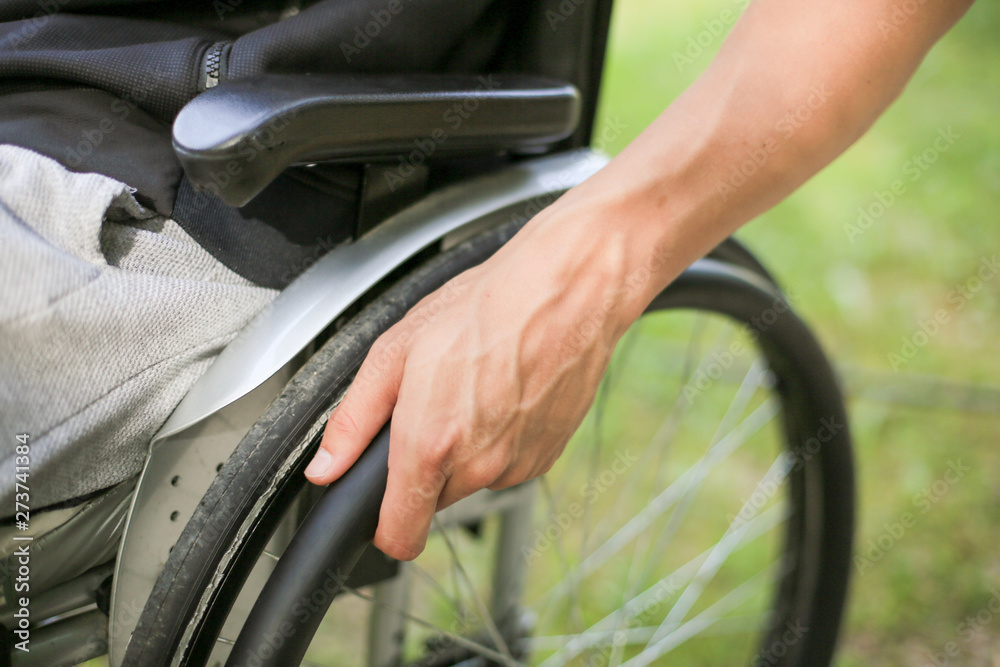 Young disabled or handicapped man sitting on a wheelchair in nature turning and holding wheels.