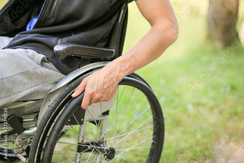 Young disabled or handicapped man sitting on a wheelchair in nature turning and holding wheels.
