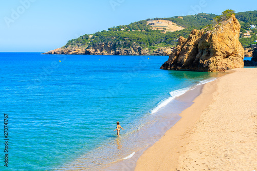Unidentified young woman walking into sea water on beautiful beach in Cala Moreta, Costa Brava, Spain