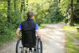 Happy and young disabled or handicapped man sitting on a wheelchair in nature turning wheels on a walking road at a beautiful sunny day