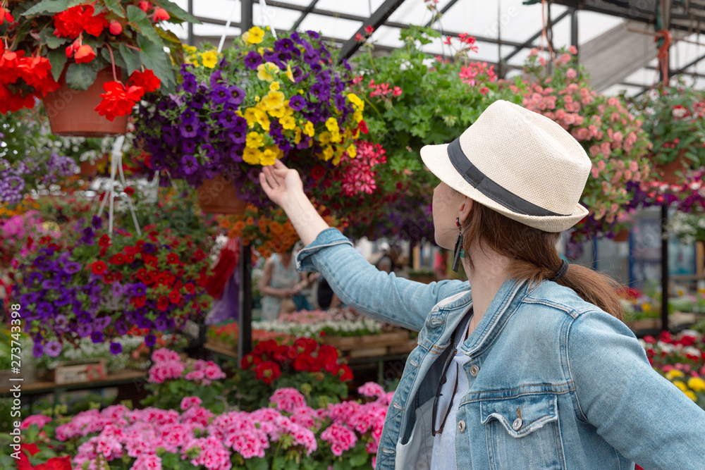  Young woman shopping in an outdoors fresh urban flowers market, buying and picking from a large variety of colorful floral bouquets during a sunny day in the city