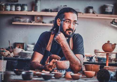 Diligent pensive man in glasses at his pottery workshop is workig for new project. photo