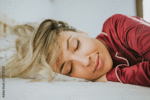 Young pretty woman in pajamas smiling while sleeping on bed in bedroom photo