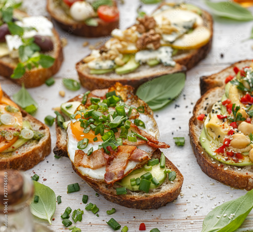 Assorted open faced sandwiches, Open avocado sandwiches made of slices of sourdough bread with various toppings  on a white wooden table. Delicious and nutritious breakfast