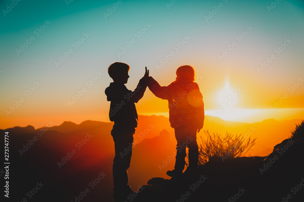 Silhouettes of happy boy and girl hiking at sunset mountains