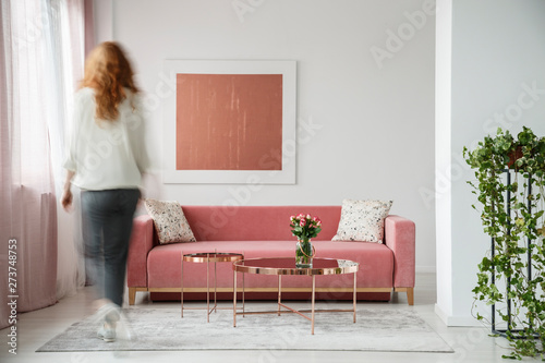 Blurry silhouette of a woman in motion in an artistic living room interior with a painting above velvet sofa, flowers and plants
