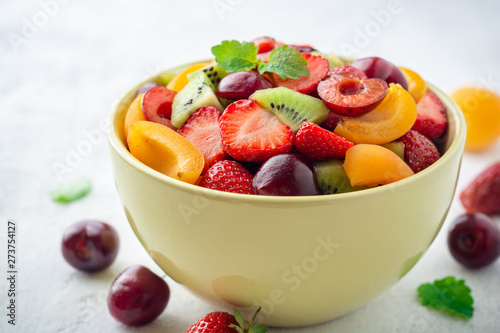 Healthy fresh fruit salad in bowl on gray concrete background. Selective focus.