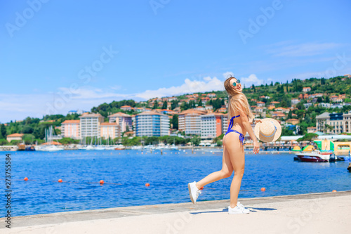 Photography Portoroz, Slovenia - Jul 6, 2018 beautiful woman has blue swimsuit, sunglasses, boater and walk at the seaside