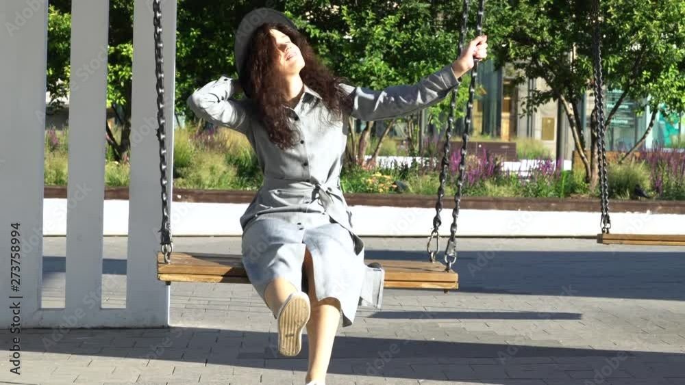 Curly girl swinging on a swing. She is wearing a black hat. Sunny morning weather. Curly girl swinging on a swing. She is wearing a black hat. Sunny morning weather.