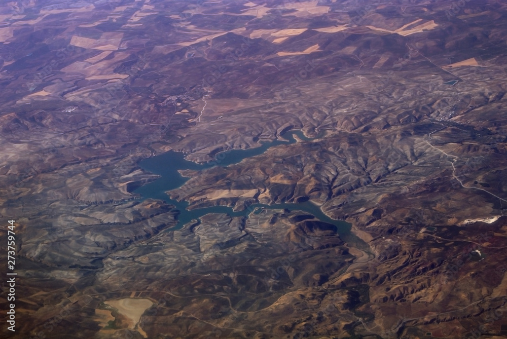 Vista áerea de ruta y paisaje de España con colinas, llanuras y ríos desde el aire durante vuelo y viaje en avión comercial.