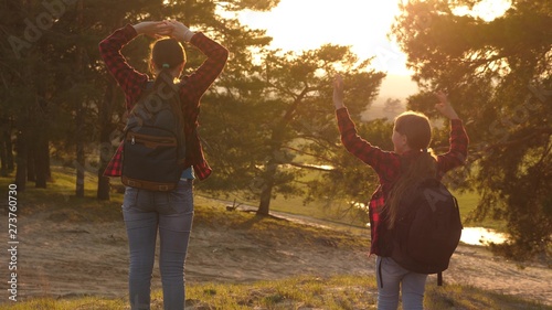 Hiker Girl. two girls travel, walk through forest and wave their hands on hill. girls travel with backpacks on country road. Happy family on vacation travels. sports tourism concept.