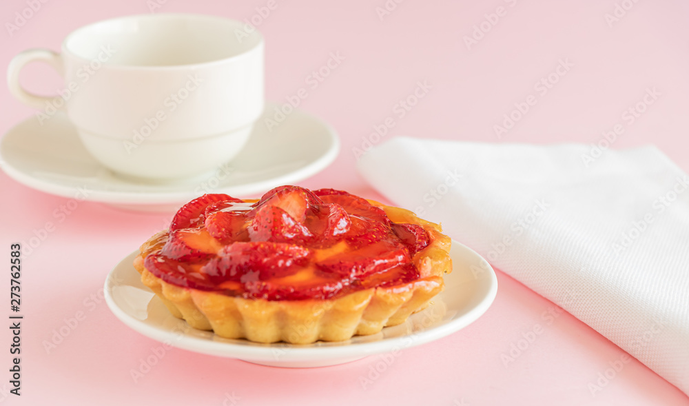 Tartalet with vanilla cream covered with slices of strawberry on the table. On the pink background is a cup of tea. Tartalet with vanilla cream covered with slices of strawberry on the table. On the pink background is a cup of tea.