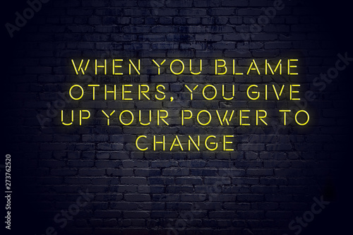 Neon sign with positive wise motivational quote against brick wall 