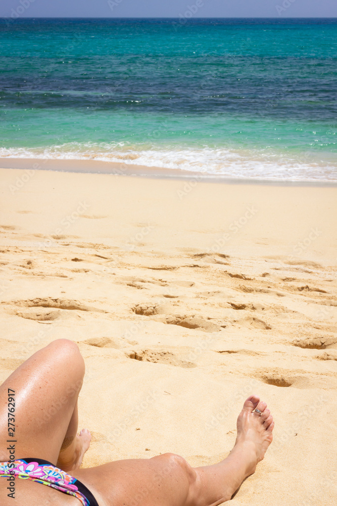 Woman legs resting on sand by turquoise water sea. Female tourist sunbathing on empty beach. Calm, relax vacation concepts Woman legs resting on sand by turquoise water sea. Female tourist sunbathing on empty beach. Calm, relax vacation concepts