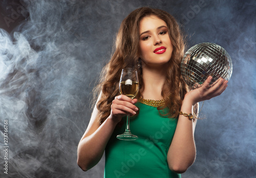 Young happy girl wearing dress holding disco ball and singing into microphone at party