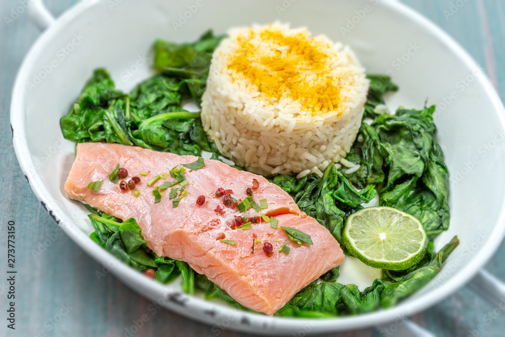 Salmon fillet with rice and spinach garnish. Fish steak. Lemon salmon on white plate on wooden background