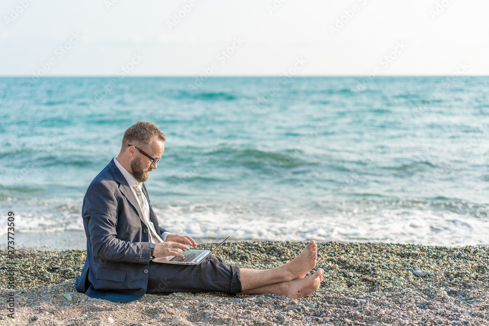 Businessman working with computer and talking on phone on the beach 