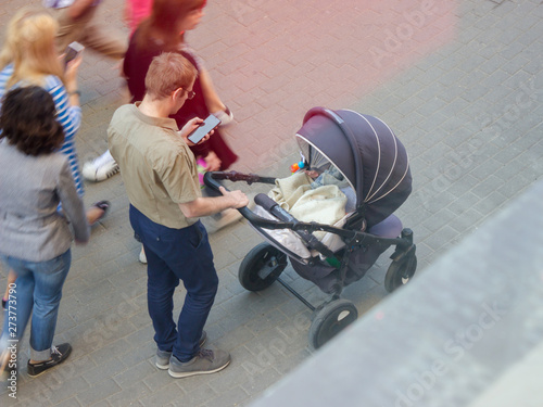 An adult male husband stands next to the stroller with a baby.