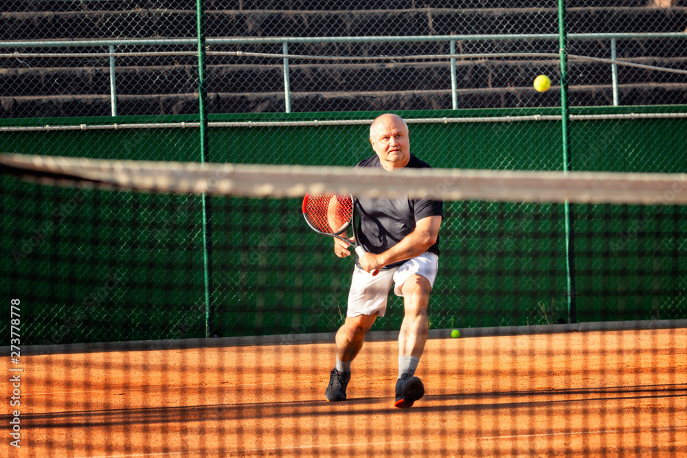 Obraz premium A middle-aged bald man emotionally plays tennis on the court. Outdoor.