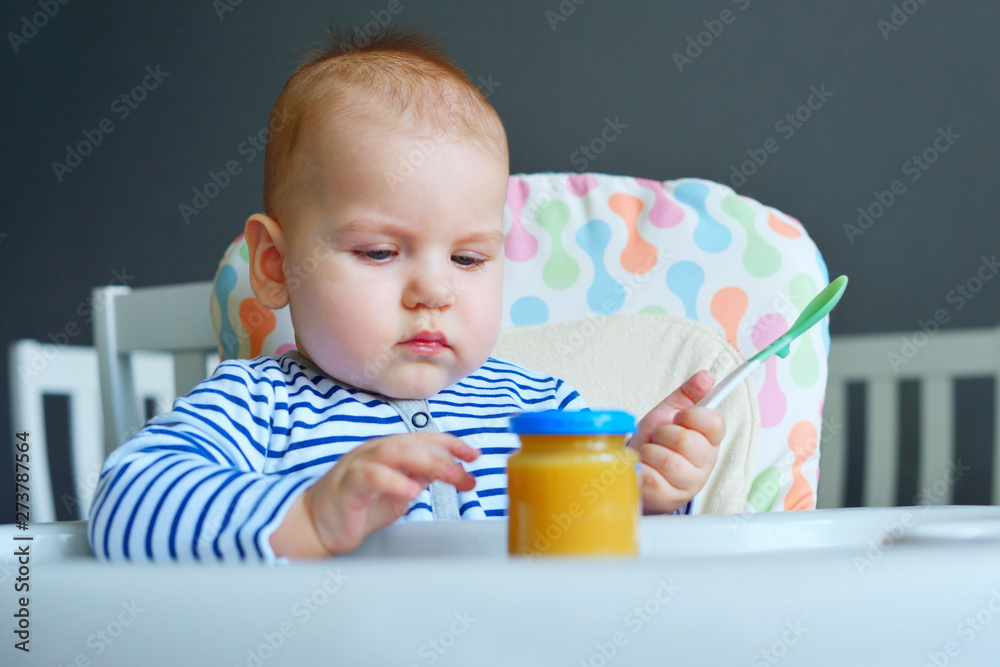 Happy boy 7-8 months eats Apple/pear puree with spoon in kitchen at home. Baby food, solid food concept. Happy boy 7-8 months eats Apple/pear puree with spoon in kitchen at home. Baby food, solid food concept.