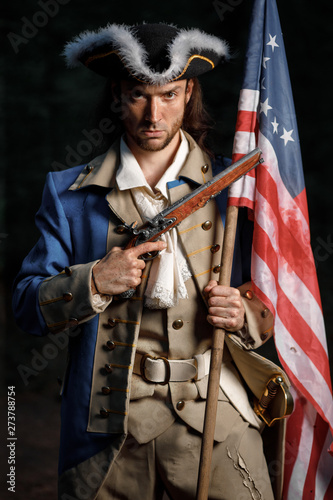 Portrait of man dressed as soldier of War of Independence United States aims from pistol with flag. 4 july independence day of USA concept photo composition: soldier and flag.