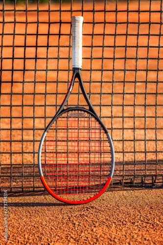Tennis racket with a ball near the net on the earthen court. Sunny day. Close-up. Vertical.