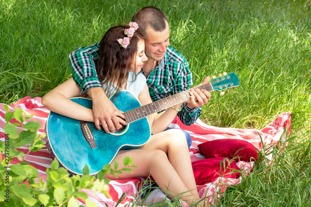 summer romantic picnic. the guy shows the girl how to play the guitar. couple sitting on the grass