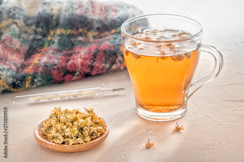 Herbal tea with pharmaceutical chamomile, warm scarf and medical thermometer on a white table